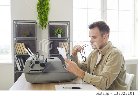Thoughtful editor reading sheet beside vintage typewriter at wooden desk by window Thoughtful editor reading sheet beside vintage typewriter at wooden desk by window 135323101