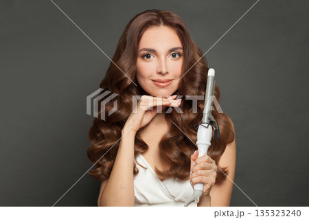 Healthy woman with long wavy hairstyle using hair curling tongs iron, indoor portrait. Healthy woman with long wavy hairstyle using hair curling tongs iron, indoor portrait. 135323240