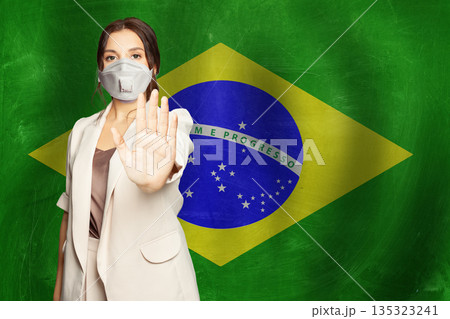 Confident woman in medical mask showing stop gesture open palm hand against flag of Brazil  135323241