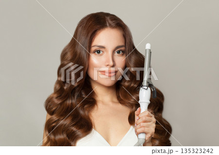 Pretty woman with long wavy hairstyle using hair curling tongs iron, indoor portrait. Pretty woman with long wavy hairstyle using hair curling tongs iron, indoor portrait. 135323242