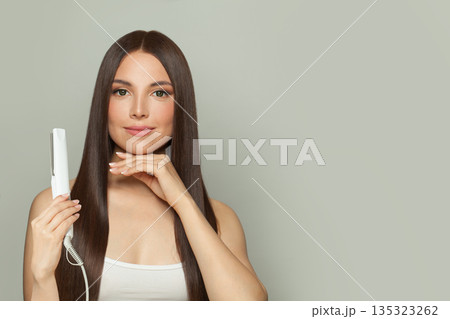Gorgeous woman brunette with long straight smooth hairstyle using hair straightener iron  135323262