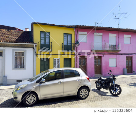 Colorful Portuguese houses with pink, yellow, and white facades, parked car and motorcycle in front 135323604