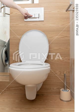 Hand pressing dual flush buttons on a ceramic wall-hung toilet, promoting hygiene and water saving in a modern bathroom 135323930
