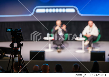 Panel discussion on stage with two speakers and camera recording audience at event conference 135324061