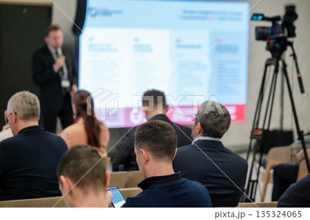 Business conference presentation with speaker, audience, and professional video setup in a modern conference hall Business conference presentation with speaker, audience, and professional video setup in a modern conference hall 135324065