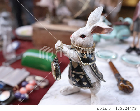 Figurine of White Rabbit holding pocket watch. Alice in Wonderland. Antique flea market in Europe, Italy. Vintage items.  135324475