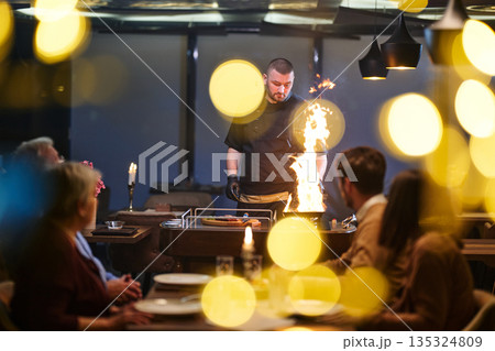 Professional Restaurant Chef Cooking Meat with Flambe Technique at Table for Guests 135324809