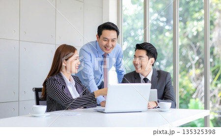 明るい会議室でノートパソコンを囲み笑顔で打ち合わせをする日本人ビジネスチーム 135325398