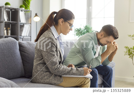 Man in therapy session with psychologist, patient sitting with gesture of stress 135325889