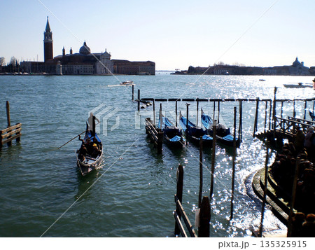 A serene gondola glides through the narrow canals of Venice, surrounded by centuries-old palaces, graceful bridges, and softly rippling water. The warm reflections of historic façades shimmer on the 135325915