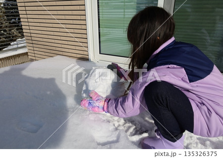 雪だるまを作る女の子、家の前で楽しむ冬のひととき 135326375