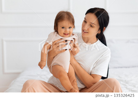 Happy baby smiling while being held by mother on bed Happy baby smiling while being held by mother on bed 135326425