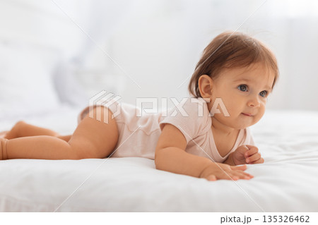 Baby lying on bed during tummy time in a bright bedroom 135326462