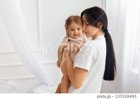 Mother holding her infant baby at home in bright minimalist interior Mother holding her infant baby at home in bright minimalist interior 135326493