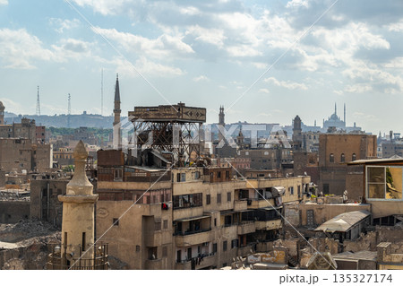 A panoramic view of Old Cairo in Egypt showcases historic buildings, minarets, and rooftops under a cloudy sky. The scene reflects the rich architectural heritage of the city. A panoramic view of Old Cairo in Egypt showcases historic buildings, minarets, and rooftops under a cloudy sky. The scene reflects the rich architectural heritage of the city. 135327174