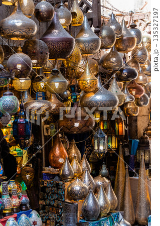 Khan el-Khalili market in Cairo features vibrant stalls filled with colorful goods. Diverse people browse the market, surrounded by traditional architecture and lively atmosphere. Khan el-Khalili market in Cairo features vibrant stalls filled with colorful goods. Diverse people browse the market, surrounded by traditional architecture and lively atmosphere. 135327197