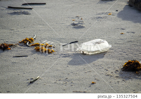 Abandoned plastic container on beach sand illustrating irresponsible waste disposal and sustainability challenges 135327504