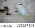 Discarded glass bottle lying on wet sand surface symbolizing urban litter pollution and careless waste disposal 135327506