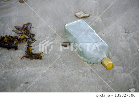 Discarded glass bottle lying on wet sand surface symbolizing urban litter pollution and careless waste disposal 135327506