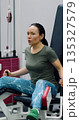 A middle-aged woman performs leg extensions with precision, focusing on building strong quadriceps during her intense gym fitness session. 135327579