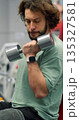 Gym workout. Close-up vertical photo of a fit bearded man training biceps with dumbbells during an intense gym workout. Seated biceps with dumbbells workout. 135327581