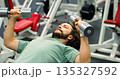 A bearded Caucasian man performs dumbbell bench presses, focusing on chest strength in detailed close-up photo. Intense workout targeting chest muscles by a focused gym-goer. 135327592
