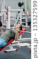 Gym workout. Photo of a middle-aged woman pushes through a bench press set on the hammer machine, combining steady breathing and firm control for an effective workout. 135327599