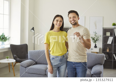 Happy young couple holding house key in hands standing in a new apartment on moving day. Happy young couple holding house key in hands standing in a new apartment on moving day. 135327911