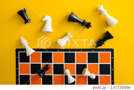 Chess pieces falling on orange board against yellow background Chess pieces falling on orange board against yellow background 135330066