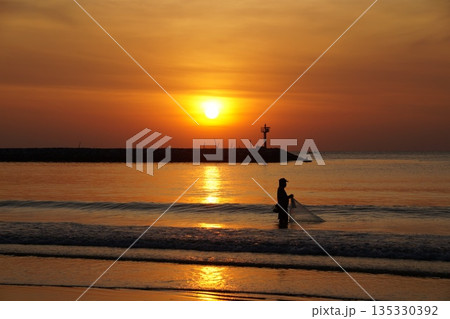 A fisherman nets fish at dawn.  135330392