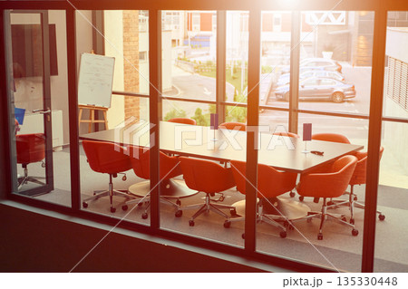 Conference room with orange chairs and large windows overlooking a parking lot in late afternoon light 135330448
