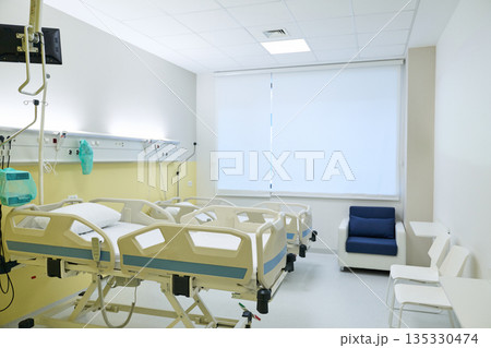 Modern hospital room with multiple patient beds and seating area during daytime Modern hospital room with multiple patient beds and seating area during daytime 135330474