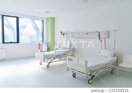 Clean hospital room with two empty beds and natural light from windows during daytime 135330515