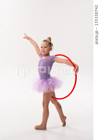 Young dancer with a cochlear implant balances with a red hoop during studio training. Inclusive performance, auditory support, and physical development through rhythmic gymnastics and ballet. 135330742