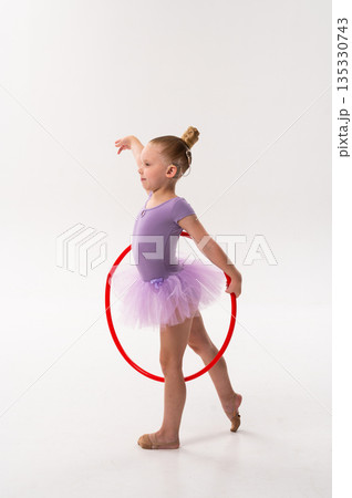 Young dancer with a cochlear implant balances with a red hoop during studio training. Inclusive performance, auditory support, and physical development through rhythmic gymnastics and ballet. 135330743