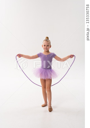 Young ballerina with a cochlear implant stretches a red hoop while posing in a lavender tutu. Inclusive gymnastics, hearing technology, and childhood coordination through rhythmic dance and movement. 135330758