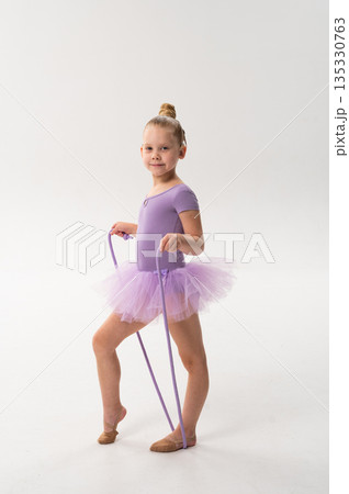 Smiling ballerina with a cochlear implant poses with a rope in a lavender tutu. Inclusive ballet, hearing technology, and confident childhood expression through rhythmic gymnastics and dance. 135330763