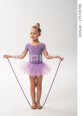 Little ballerina with a cochlear implant holds a purple rope while standing in a ballet pose. Inclusive sport, hearing technology, and childhood coordination through dance and rhythmic gymnastics. Little ballerina with a cochlear implant holds a purple rope while standing in a ballet pose. Inclusive sport, hearing technology, and childhood coordination through dance and rhythmic gymnastics. 135330786