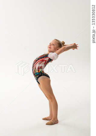 Young rhythmic gymnast with cochlear implant posing in training leotard in studio. Hearing rehabilitation, inclusive childhood sport and body awareness through flexibility and balance 135330812
