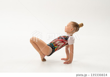 Young rhythmic gymnast with cochlear implant posing in training leotard in studio. Hearing rehabilitation, inclusive childhood sport and body awareness through flexibility and balance 135330814