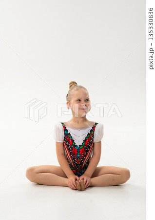 Young rhythmic gymnast with cochlear implant posing in training leotard in studio. Hearing rehabilitation, inclusive childhood sport and body awareness through flexibility and balance 135330836
