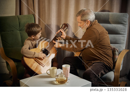 Senior man teaching boy guitar at home living room. 135331028