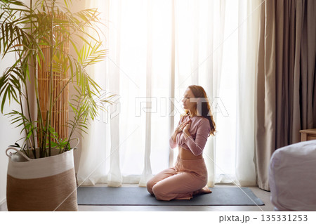 Calm adult caucasian woman meditating on yoga mat in hotel room 135331253