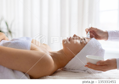 Therapist applying cosmetic clay mask with brush to relaxed woman at spa Therapist applying cosmetic clay mask with brush to relaxed woman at spa 135331451