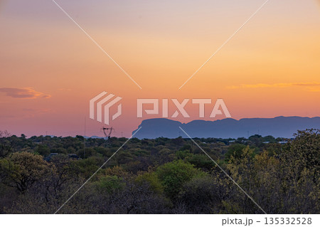 Orange and purple sunset sky over silhouetted mountains and green bushland Orange and purple sunset sky over silhouetted mountains and green bushland 135332528