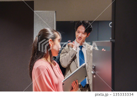 オフィスのロッカーで会話をする男女の会社員 オフィスのロッカーで会話をする男女の会社員 135333334