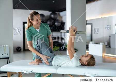 Child performing strengthening exercise with therapist support 135333520