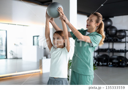 Woman therapist and child holding ball overhead Woman therapist and child holding ball overhead 135333559