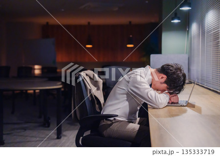 夜遅くまで仕事をしてオフィスで寝落ちをしてしまう男性 135333719