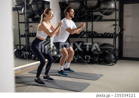 Two young people exercising in the gym in squatting position Two young people exercising in the gym in squatting position 135334121